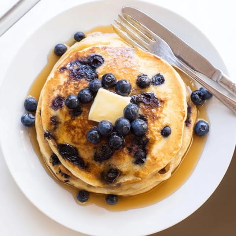 Golden-brown Blueberry Pancakes stacked high, dripping with maple syrup and a melting pat of butter for breakfast.