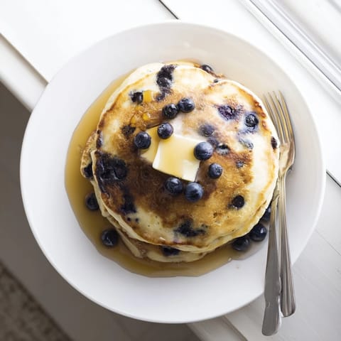 Fluffy homemade Blueberry Pancakes cooked on a griddle, topped with fresh berries and warm syrup, ready to eat.