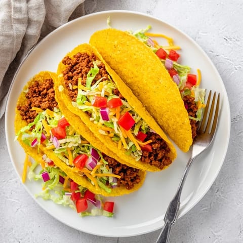 Crispy American-Style Tacos loaded with seasoned ground beef, shredded cheese, and zesty salsa for a festive meal.