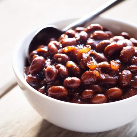Comforting Baked Beans bubbling in a Dutch oven, featuring tender navy beans coated in a thick, smoky-sweet tomato sauce.