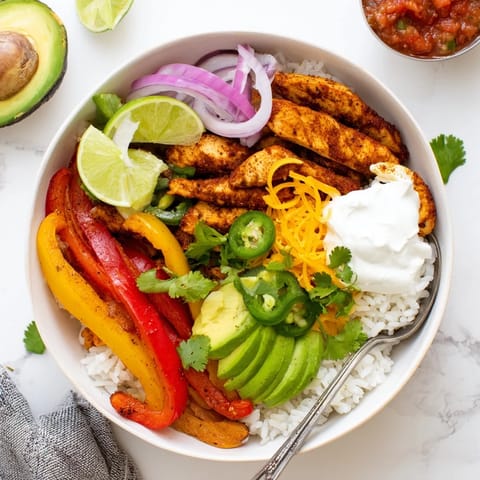 A hearty serving of Chicken Fajita Bowl featuring juicy chicken strips, sautéed veggies, and melted cheese with lime on the side.