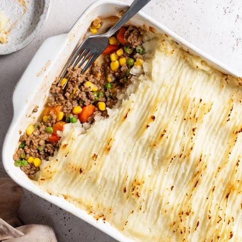Rustic casserole of seasoned ground meat and mixed vegetables topped with ridged mashed potatoes, served steaming hot for dinner.