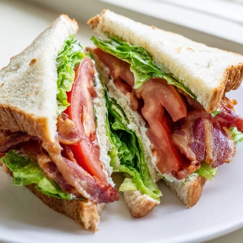 Golden brown toasted bread stacks crispy bacon, juicy tomato slices, and fresh lettuce with creamy mayonnaise.