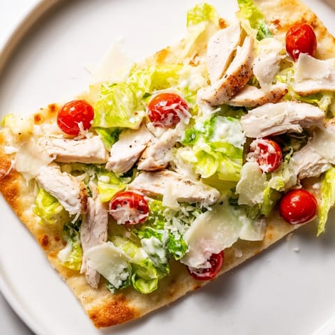 Freshly grated Parmesan and cherry tomatoes top this Caesar Chicken Flatbread, served on a rustic wooden board.