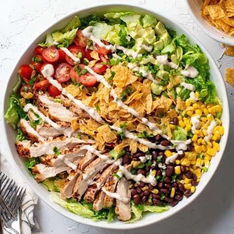 A vibrant bowl of Crunchy Taco Chicken Salad with creamy avocado and a drizzle of lime dressing.