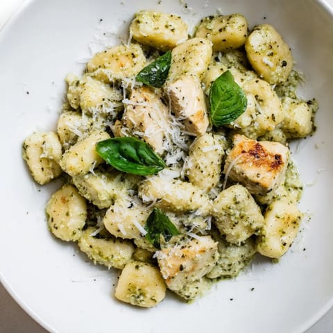 Golden pan-crisped gnocchi and juicy chicken bites coated in a rich, vibrant green pesto cream sauce, ready to serve.  