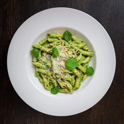 Creamy Sunflower Seed Pesto Pasta twirled on a fork with fresh basil leaves, a rustic wooden backdrop.
