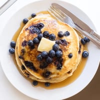 Golden-brown Blueberry Pancakes stacked high, dripping with maple syrup and a melting pat of butter for breakfast.