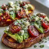 Golden roasted sweet potato toast slices topped with fresh avocado and vibrant cherry tomatoes for a savory breakfast.