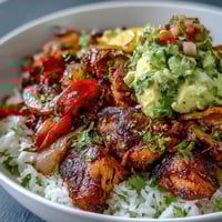 Golden-brown Sheet Pan Chicken Tinga Bowl with fluffy rice, smoky chipotle chicken, and colorful roasted peppers topped with chunky avocado salsa.